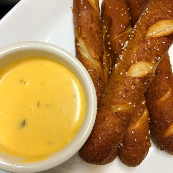Salted pretzel sticks with a side of creamy yellow cheese dip on a white plate.