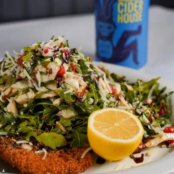 Breaded cutlet topped with arugula salad, cheese, and balsamic glaze, with a lemon half.