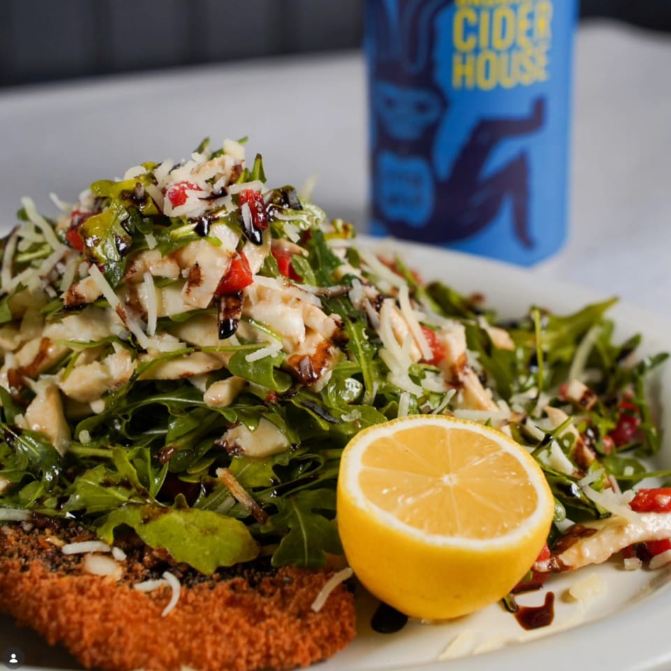 Breaded cutlet topped with arugula salad, cheese, and balsamic glaze, with a lemon half.